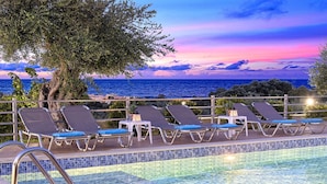 A poolside area with lounge chairs and a view of the sea at sunset. - Modern Villa With Heated Swimming Pool in Georgioupoli Greece (Apokoronas)