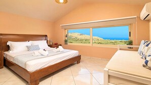 A bedroom with a wooden bed, a bedside table, a nightstand, a window with a view of the landscape, and an air conditioning unit. - Modern Villa With Heated Swimming Pool in Georgioupoli Greece (Apokoronas)
