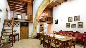 A rustic interior with a wooden dining table, chairs, a red sofa, and a loft area with a wooden staircase. - Villa in Crete With Vineyard Experience (Apokoronas)