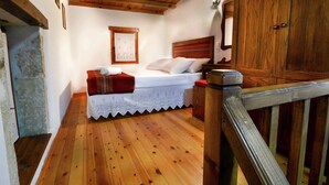 A wooden-floored bedroom with a bed, a red bench, and a wooden wardrobe. - Villa in Crete With Vineyard Experience (Apokoronas)