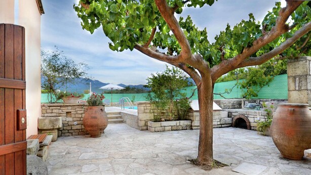 A stone patio with a tree, large pots, and a stone wall. - Villa in Crete With Vineyard Experience (Apokoronas)