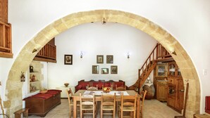 A dining area with a stone arch, wooden furniture, and a staircase. - Villa in Crete With Vineyard Experience (Apokoronas)
