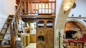 A rustic kitchen with wooden cabinets, a stone fireplace, and a wooden staircase. - Villa in Crete With Vineyard Experience (Apokoronas)