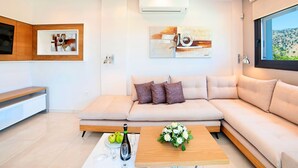 A modern living room with a beige sectional sofa, a wooden coffee table with a bottle and glasses, and artwork on the walls. - 2 new Villas With Heated Pool, Rent Separately or Together at Kournas Lake (Apokoronas)