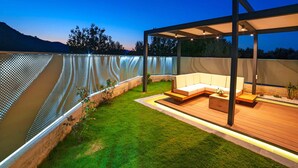 A modern outdoor patio with a wooden deck, a built-in seating area, and a decorative metal fence. - 2 new Villas With Heated Pool, Rent Separately or Together at Kournas Lake (Apokoronas)