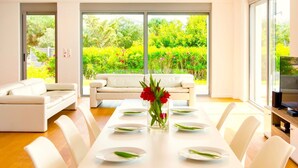 A modern living room with a dining area, large windows, a sofa, and a TV. - Sparkling Villa in Acrotiri with Private Pool near Sea Beach (Chania)