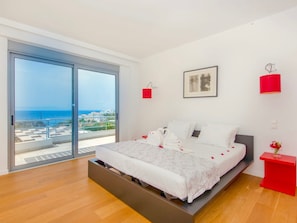 Une chambre moderne avec un grand lit, une porte-fenêtre coulissante donnant sur un balcon et une vue sur la mer.