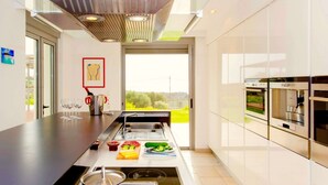 A modern kitchen with a central island, built-in ovens, and a large window offering a view of greenery. - Sparkling Villa in Acrotiri with Private Pool near Sea Beach (Chania)