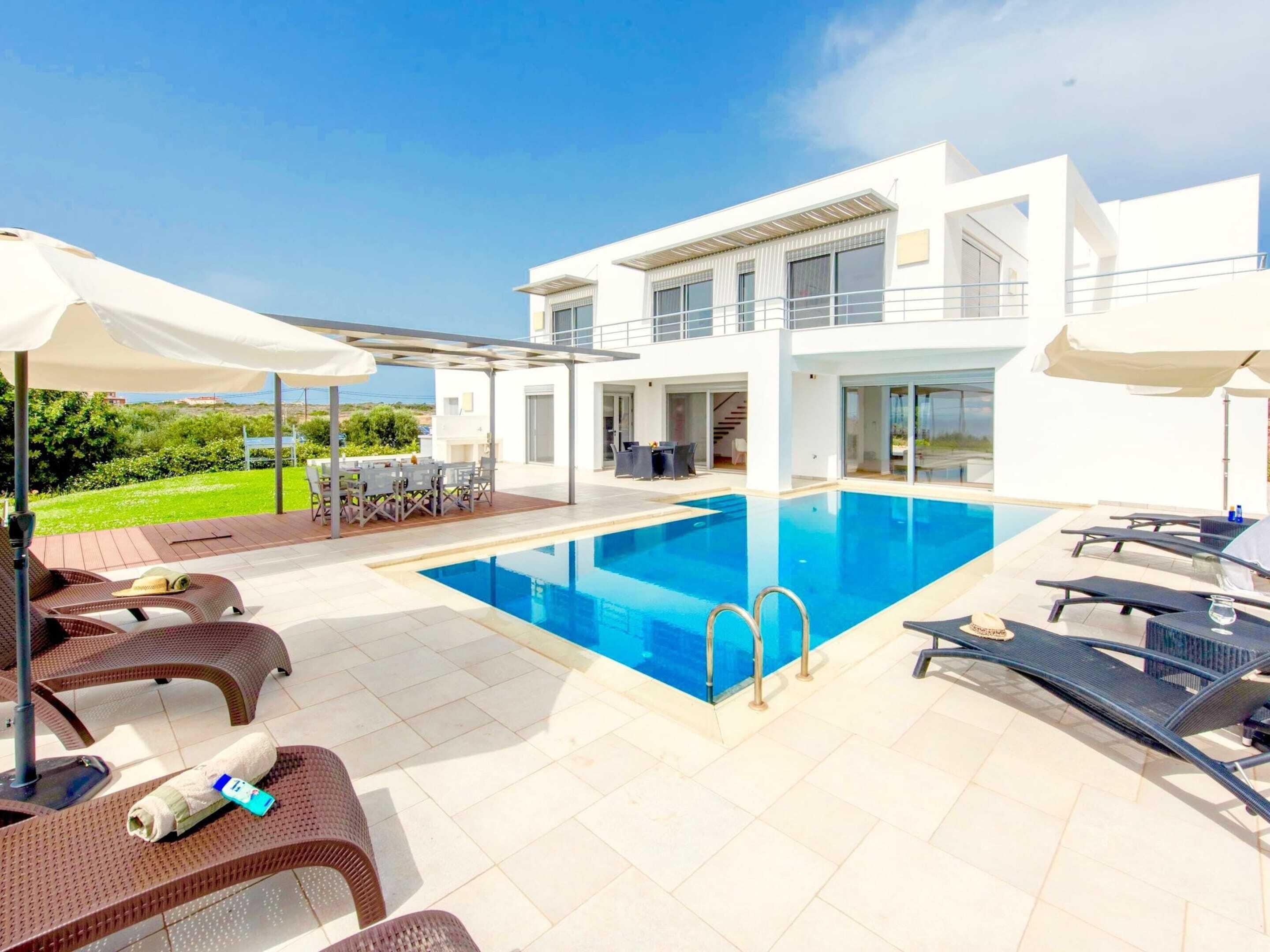 A modern poolside area with lounge chairs and umbrellas, a clear blue pool, and a white building with large windows.