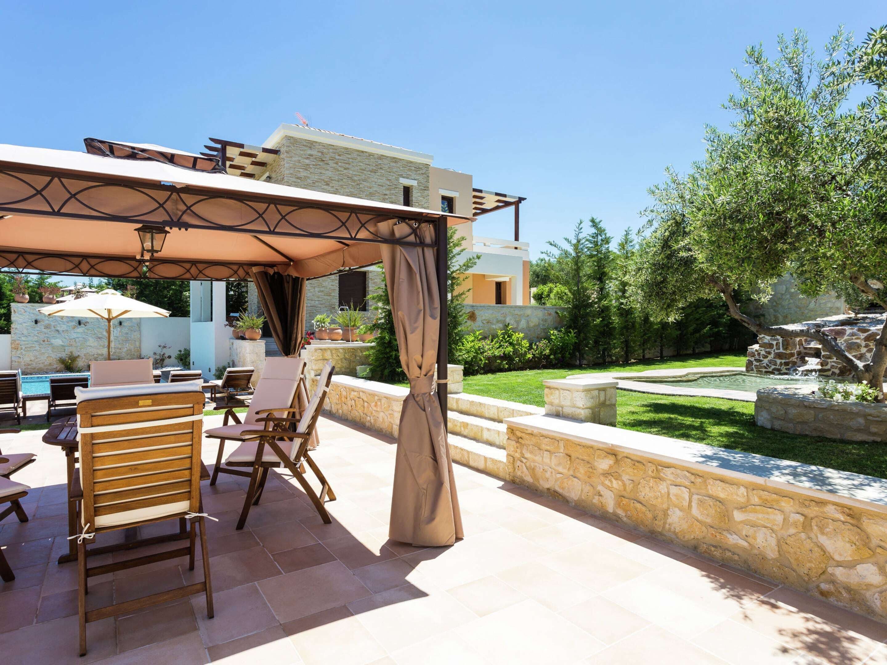 Un espace extérieur aménagé en terrasse, avec des chaises et une table en bois, des murs en pierre et une piscine.