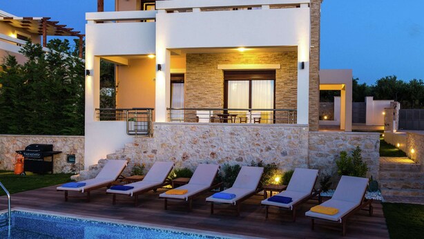 A modern two-story building with a pool area featuring lounge chairs and a stone wall. - Villa with Private Pool near Sea & Arkadi Monastery on NW Coast (Rethymno)