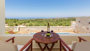 A wooden table with two chairs, a bottle of wine, and a glass of red wine on a balcony overlooking a pool and a scenic landscape. - Villa with Private Pool near Sea & Arkadi Monastery on NW Coast (Rethymno)