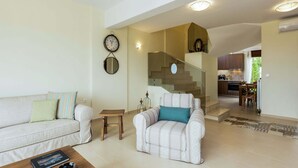 Ein Wohnzimmer mit Sofa, Sesseln, Couchtisch und einer Treppe, die in eine Küche führt.