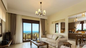 A spacious living room with a sofa, coffee table, and a television. There is a balcony with a view of the sea. - Novel Villa in Roupes with Private Pool near Arkadi Monastery (Rethymno)