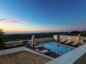 A rooftop pool with lounge chairs and umbrellas, surrounded by stone walls and overlooking a scenic landscape. - Novel Villa in Roupes with Private Pool near Arkadi Monastery (Rethymno)