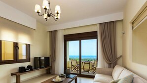 A modern living room with a sofa, a coffee table, a TV, and a balcony with a view. - Novel Villa in Roupes with Private Pool near Arkadi Monastery (Rethymno)