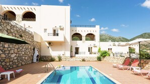 Ein Poolbereich mit klarem, blauem Pool, Steinwänden und einem weißes Gebäude mit Balkonen.