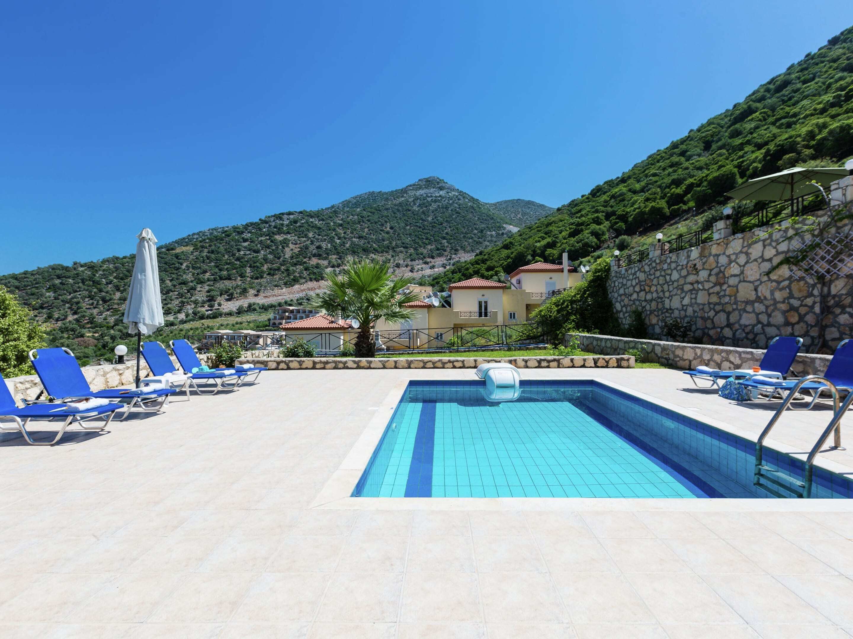 Un área de piscina con sillas reclinables azules y una pared de piedra.
