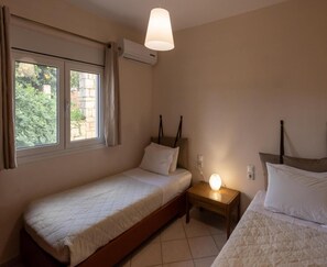 A bedroom with two beds, a window with curtains, an air conditioning unit, and a bedside lamp. - Villa in Crete With Pool & Olive Grove Views (Mylopotamos)