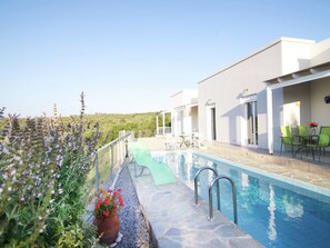 Uma piscina no terraço com um deck de pedra, uma espreguiçadeira e uma mesa com cadeiras.