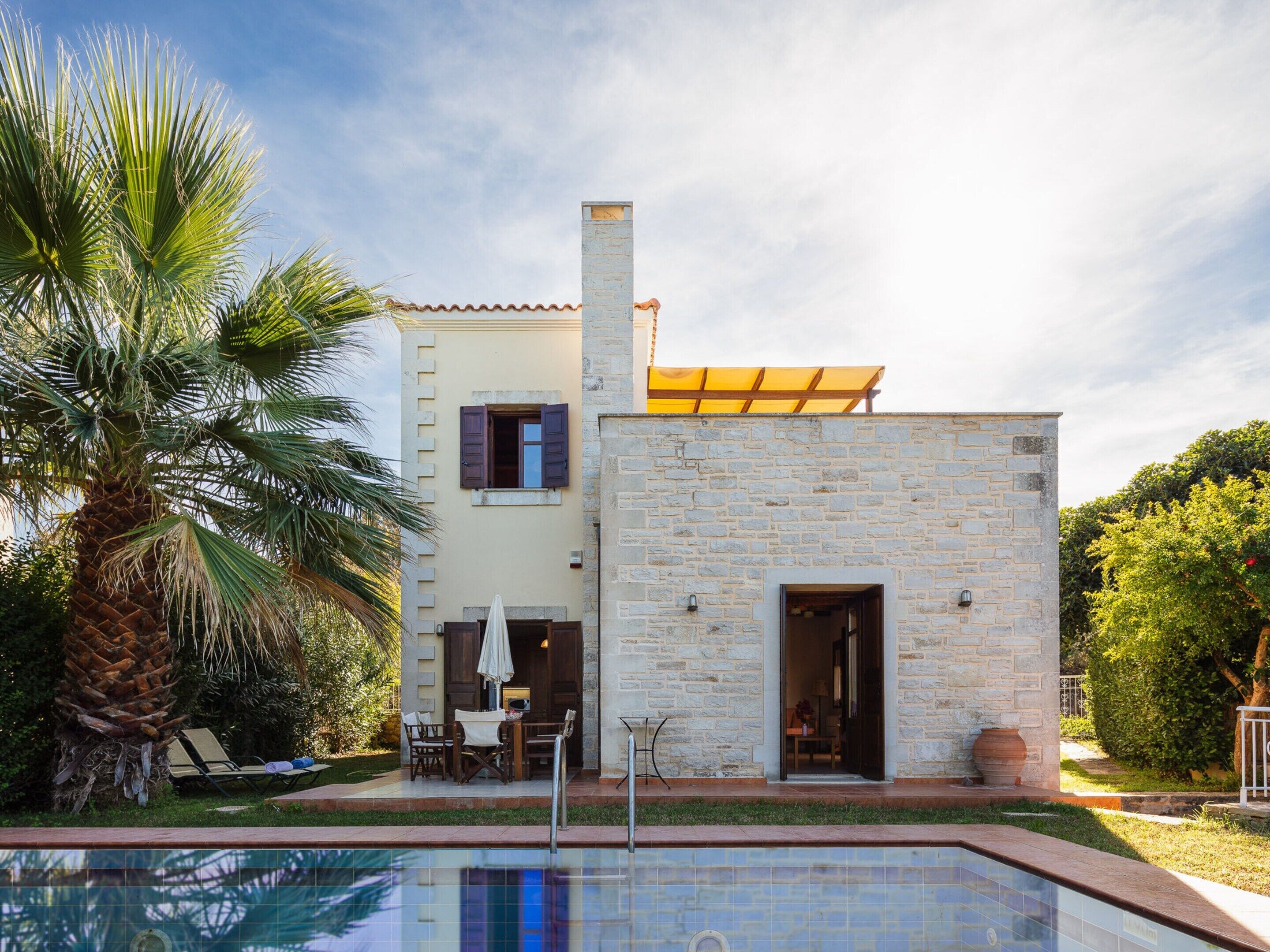 Une maison moderne à deux étages, dotée d’une façade en pierre, d’une piscine et d’un patio aménagé avec du mobilier d’extérieur.