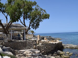 A stone structure near a beach with a covered outdoor seating area and a view of the sea.