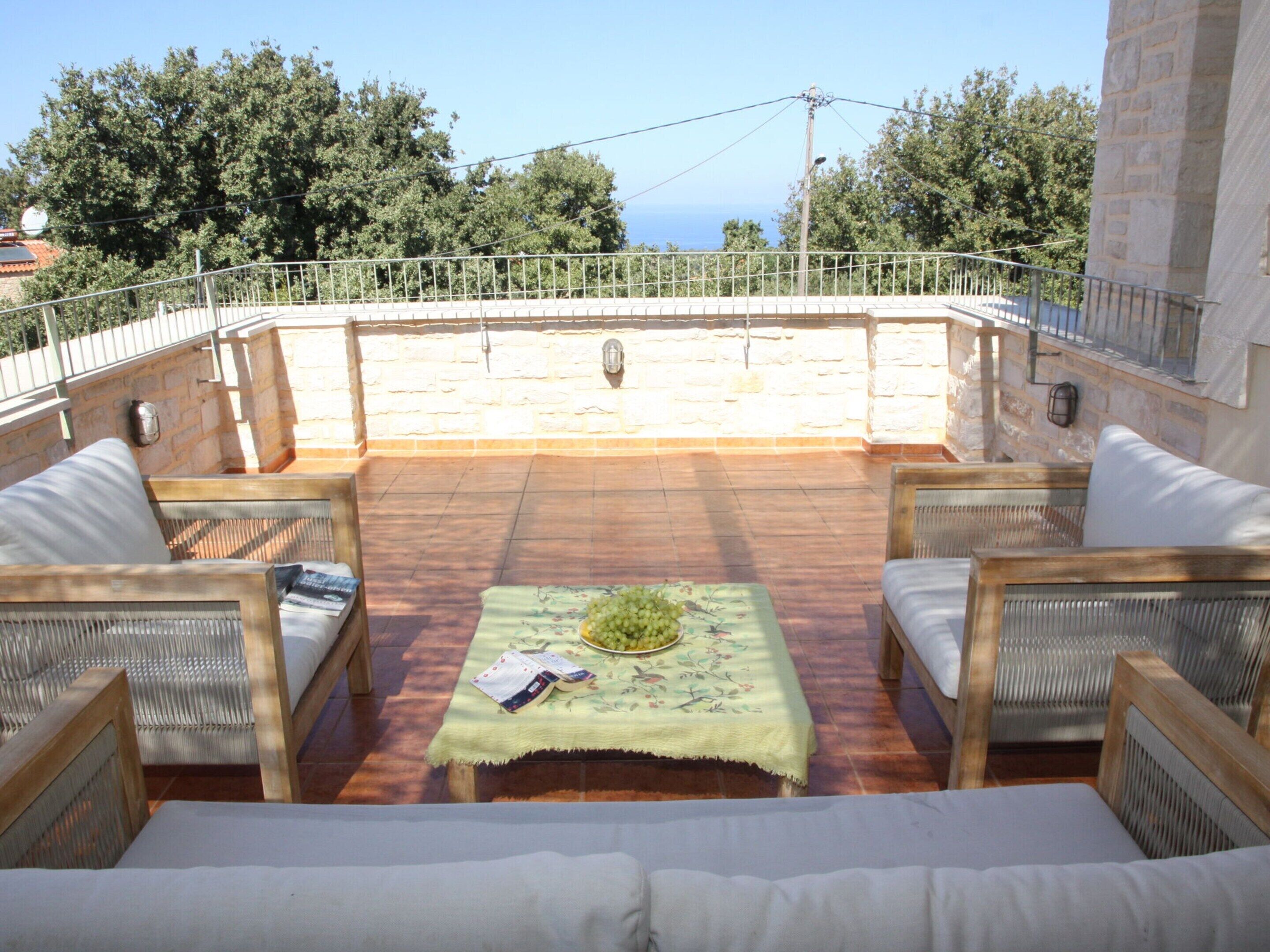 A sunlit outdoor seating area with a table, chairs, and a view of the sea.