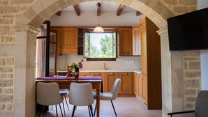 Eine Küche mit Holzausstattung, einem Esstisch mit Stühlen, einem Fenster und einem steinernen Bogen.