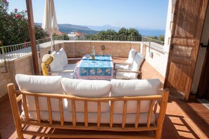 A terrace with a wooden bench and table, a view of the sea, and a stone wall.