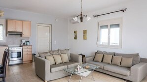 A living room with a sofa set, a glass coffee table, and a kitchen area with cabinets and a stove. - Spacious Villa in Arkadi with Swimming Pool near Sea (Rethymno)