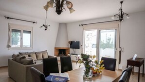 A modern living room with a sofa, dining table, chairs, a fireplace, and a TV. - Spacious Villa in Arkadi with Swimming Pool near Sea (Rethymno)