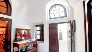 A room with a wooden desk, books, a vase with flowers, and a large arched window. - Extravagant Villa in Megalochori (Santorini)