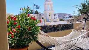 A white building with a clock tower, a flag, and a hammock on a balcony. - Extravagant Villa in Megalochori (Santorini)