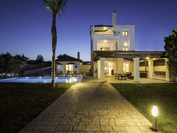 A modern two-story house with a swimming pool, outdoor seating, and a well-lit patio area.