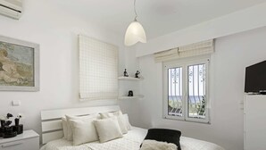 A bedroom with a bed, bedside tables, a TV, a window with a view, and a painting on the wall. - Villa on Island With Private Pool (Rhodes)