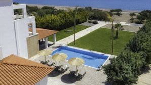 A pool area with a view of the sea, surrounded by greenery and a white building. - Villa on Island With Private Pool (Rhodes)