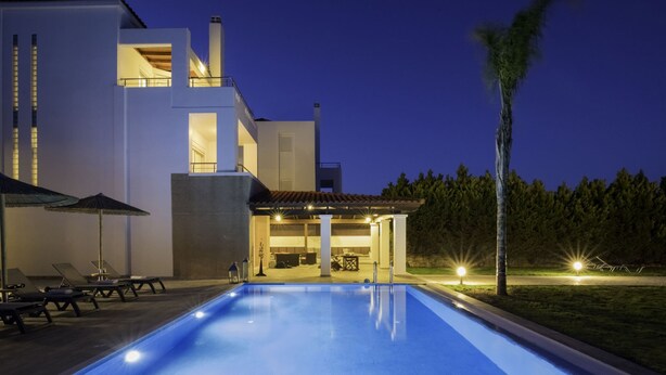 A modern pool area with lounge chairs and umbrellas, surrounded by a two-story building with large windows and a covered patio. - Villa on Island With Private Pool (Rhodes)