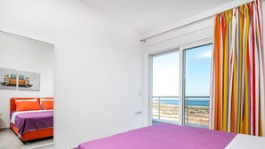 Een slaapkamer met een bed, een raam met uitzicht op zee, en een kleurrijk gordijn.