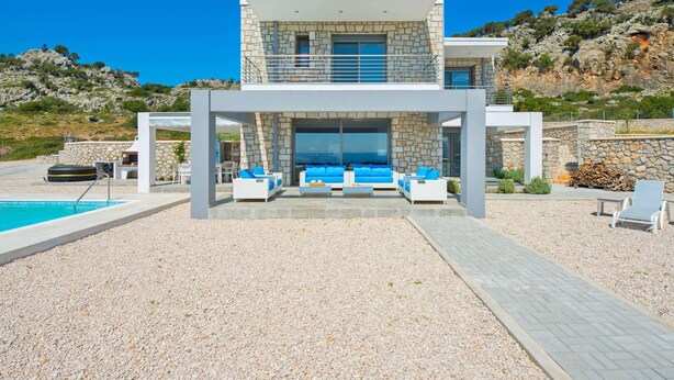 A modern two-story house with a stone facade, a pool, and outdoor seating. - Villa in Rhodes With Infinity Pool & Sea Views (Rhodes)