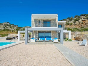 Una casa moderna de dos pisos con fachada de piedra, piscina y mobiliario de exterior.