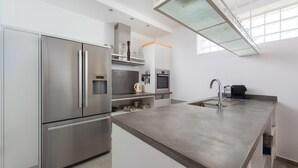 A modern kitchen with stainless steel appliances, a large island with a sink, and a mezzanine with glass railings. - Villa in Rhodes With Infinity Pool & Sea Views (Rhodes)