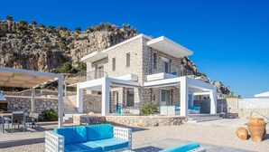 A modern stone house with a balcony, outdoor seating area, and a view of rocky cliffs. - Villa in Rhodes With Infinity Pool & BBQ (Rhodes)