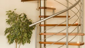 A spiral staircase with wooden steps and metal railings, a potted plant beside it, and a lit candle on the top step.