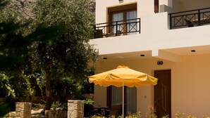 A two-story building with a pool, blue lounge chairs, and an umbrella.