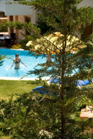Ein Poolbereich mit einer Person, die schwimmt, umgeben von Grünflächen und einem Gebäude im Hintergrund.