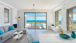 Ein modernes Wohnzimmer mit einer Couch, einem Esstisch und Stühlen, ein Balkon mit Meerblick und einer Steinwand.