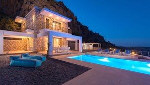 Ein modernes, zweistöckiges Haus mit Natursteinfassade, einem Swimmingpool und Sitzgelegenheiten im Freien.