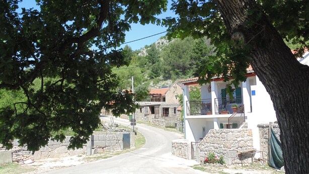 Uma estrada estreita serpenteando por uma área residencial com muros de pedra e casas.
