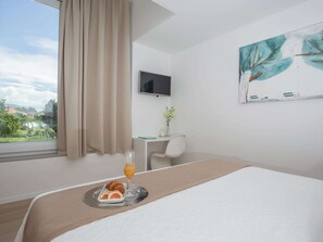 Ein Hotelzimmer mit einem Bett, einem Schreibtisch, einem Sessel, einem Fernseher und einem Bild an der Wand.