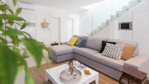 Een moderne woonkamer met een grijze hoekbank, een salontafel en een trap met glazen balustrades.